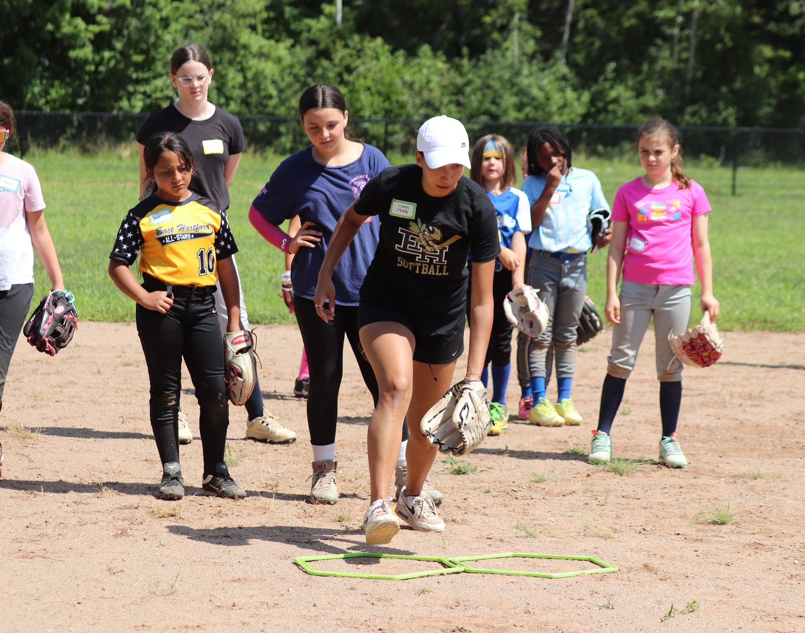 A coach leads footwork drills through agility rings as players watch at an EHSB clinic.